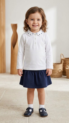 Bambina con polo bianca ricamata a cuori e gonna blu